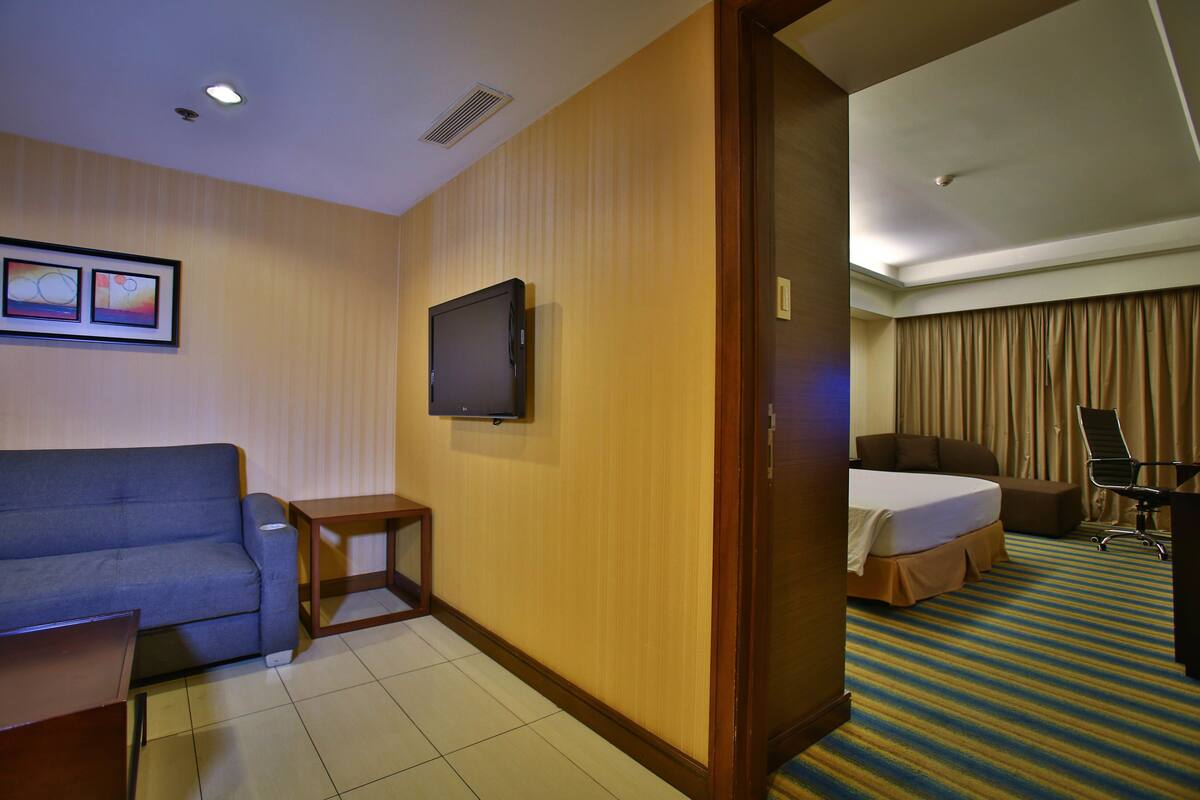 A hotel room with a sofa, a TV, a desk, and a bed.