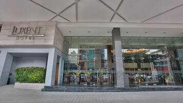L’extérieur de l’hôtel Luxent se distingue par sa façade moderne en verre, un espace paysager agrémenté de plantes et une vue dégagée sur l’intérieur à travers le verre.