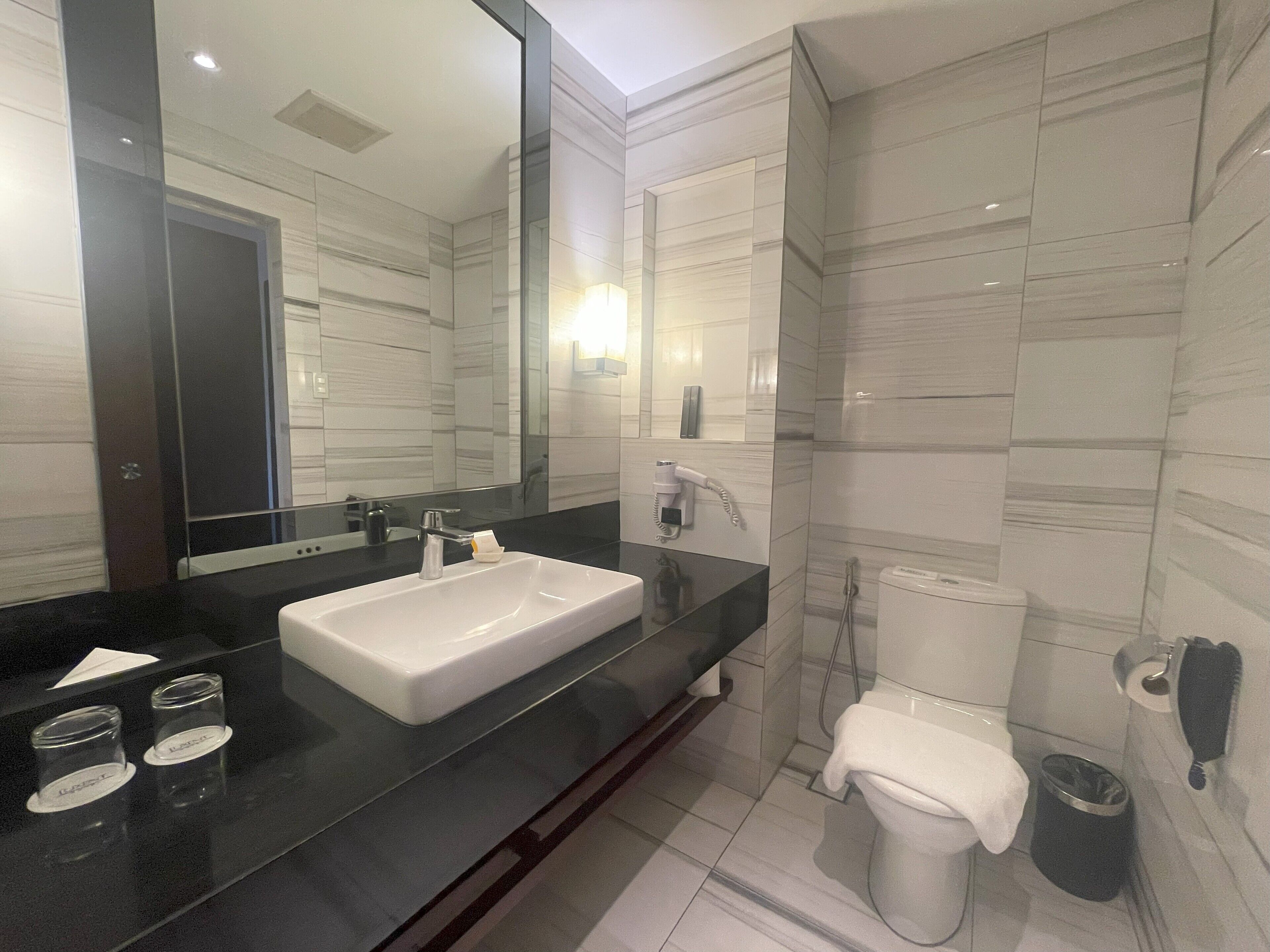 A modern bathroom with a large mirror, a white sink, a toilet, and a shower area.