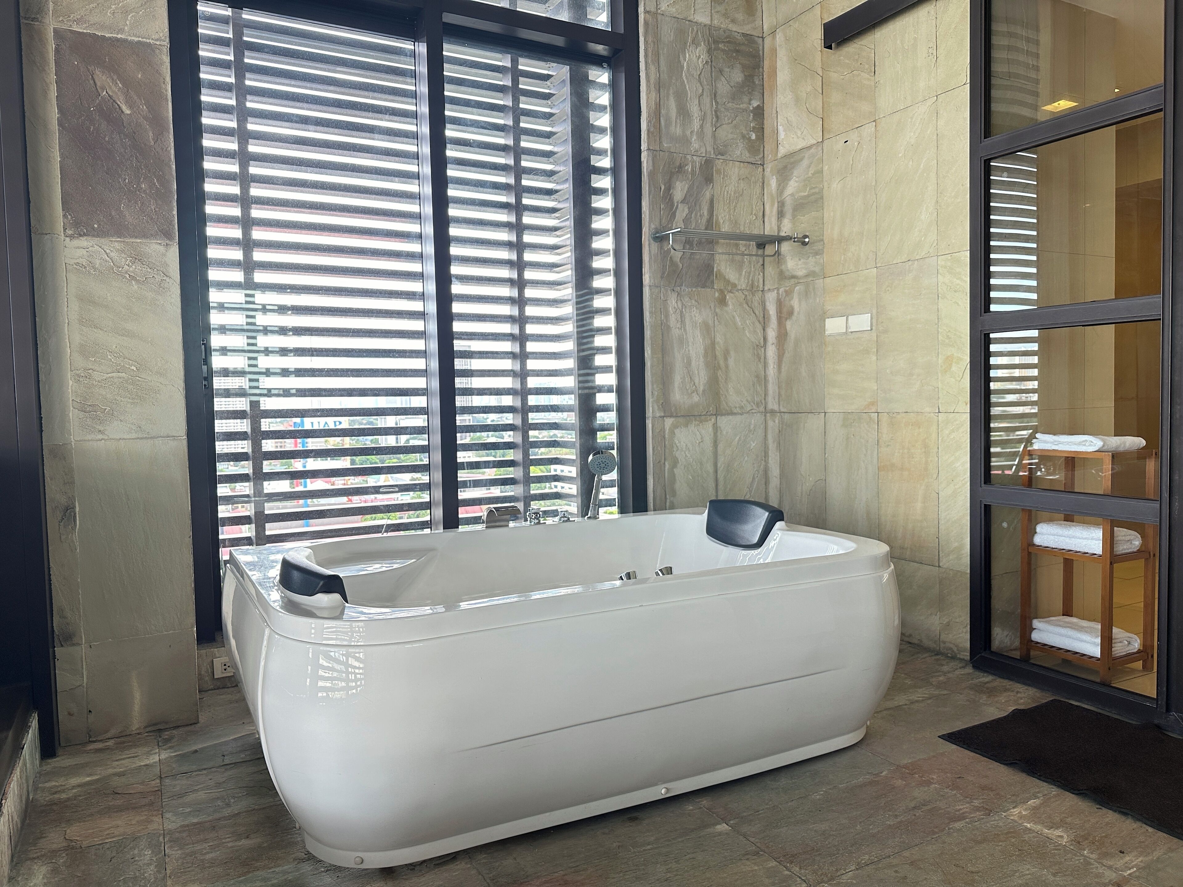 Un baño moderno con una bañera grande, un box de ducha de vidrio y vistas de la ciudad a través de ventanales del piso al techo.