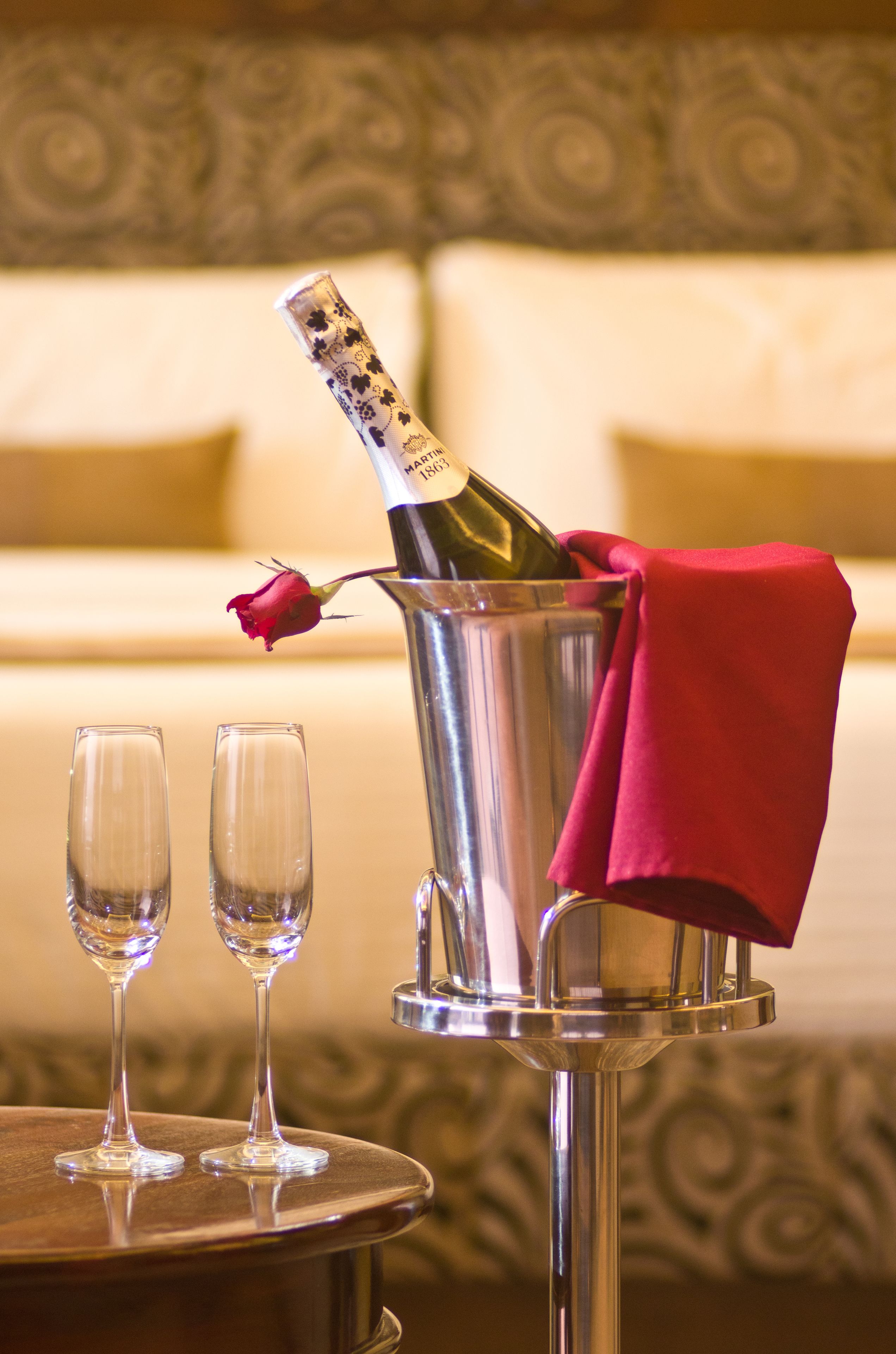 A champagne bottle in a metal bucket with a red rose and two glasses on a table.