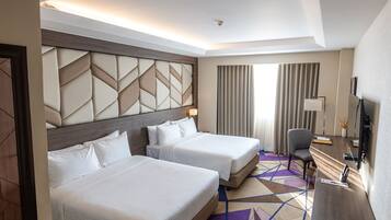 A hotel room with two beds, a desk, a chair, and a TV.