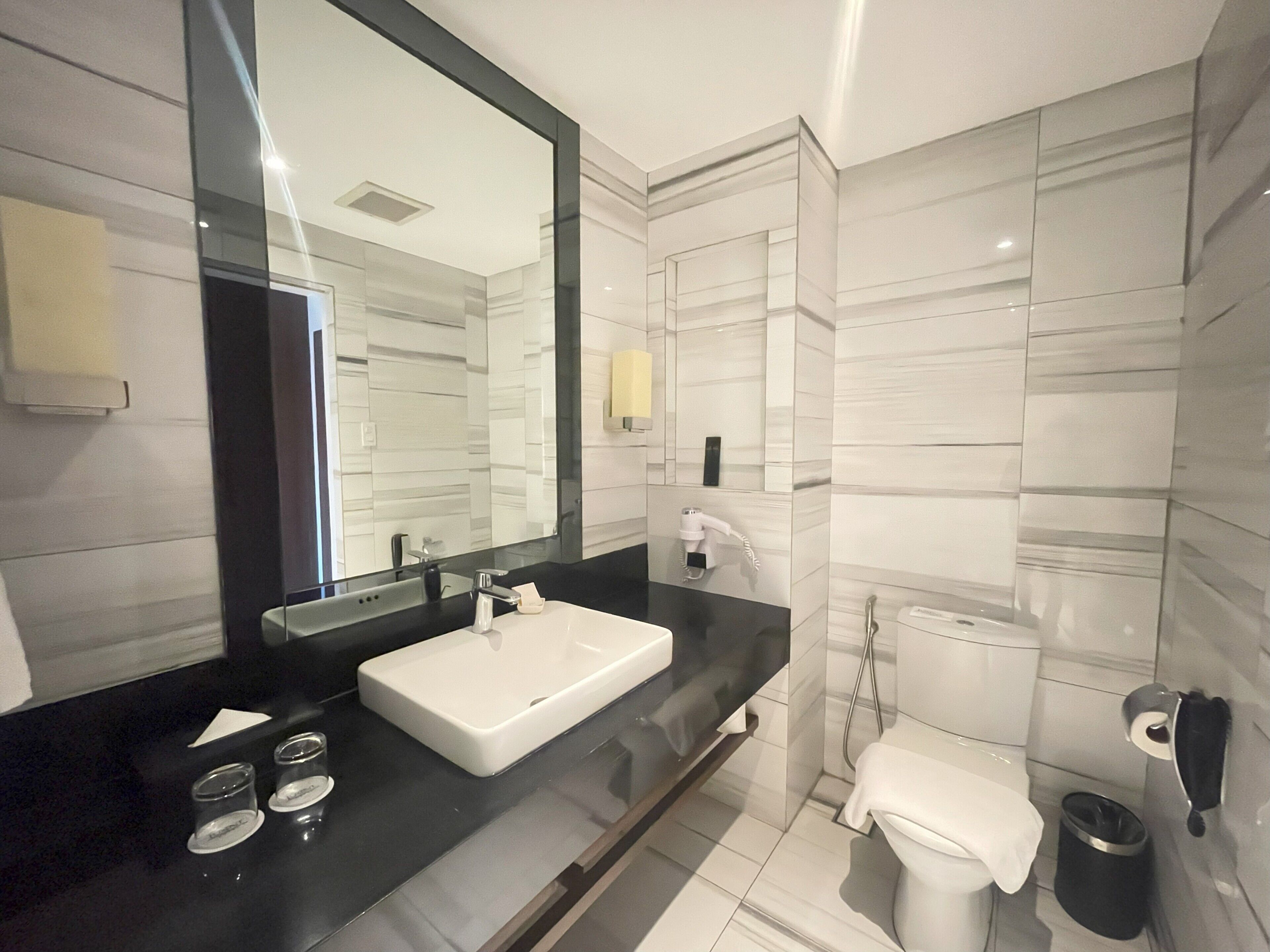 A modern bathroom with a large mirror, a white sink, a toilet, and a shower.