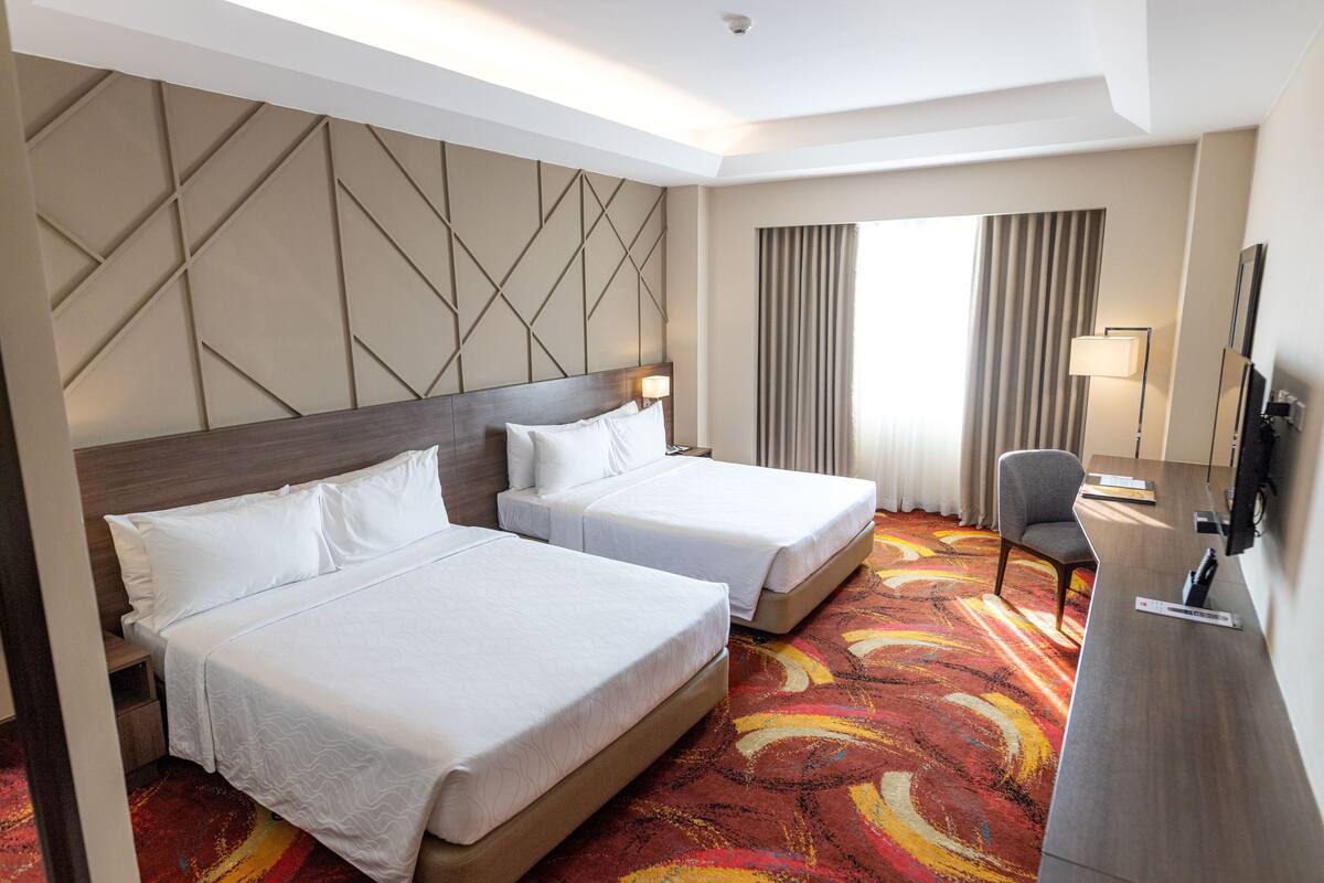A hotel room with two beds, a desk, a chair, and a television.