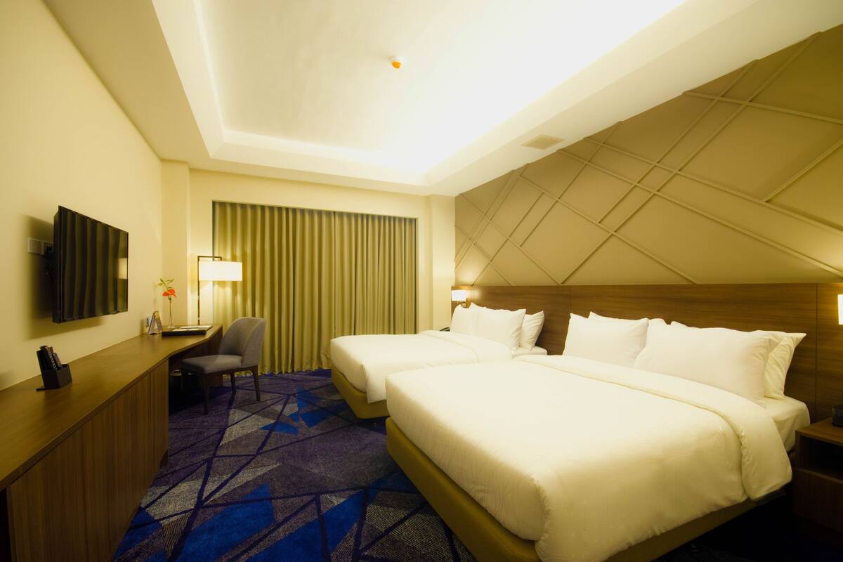 A hotel room with two beds, a desk, a chair, a TV, and a patterned carpet.