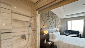 A hotel room with a large bed, a shower, a nightstand, and a view of the city through a window. - Luxent Hotel (Quezon City)