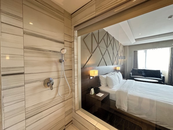 A hotel room with a large bed, a shower, a nightstand, and a view of the city through a window.