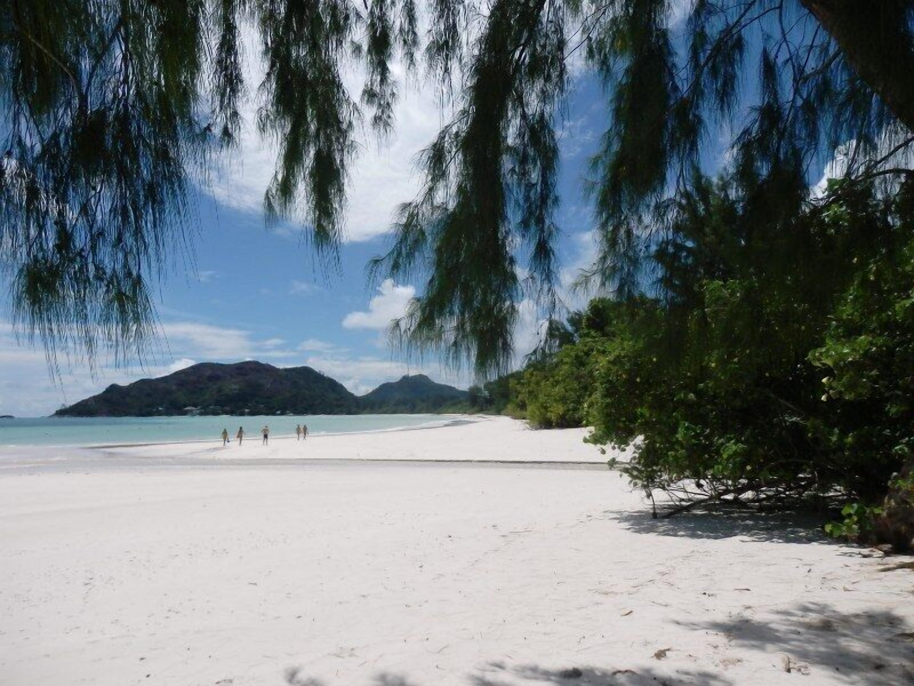 A beach with white sand, a few people walking, and a mountain in the background.