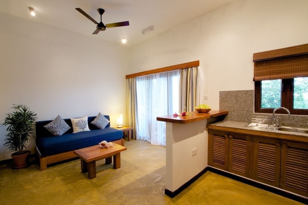 A compact living space with a sofa, a small table, a kitchen area with a sink, and a ceiling fan.