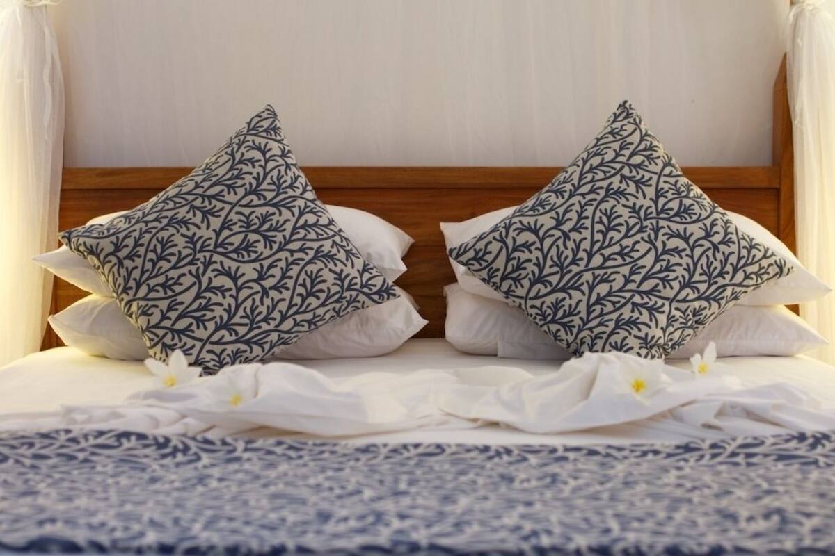 Ein Bett mit hölzernem Kopfteil, zwei dekorative Kissen mit Blattmuster und einer weißen Bettdecke.