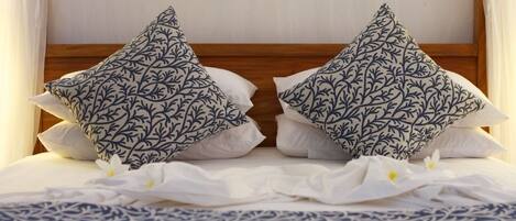 Uma cama com cabeceira de madeira, duas almofadas decorativas com padrão de folhas e um edredom branco.