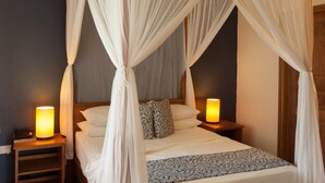 A four-poster canopy bed with a wooden frame, two bedside tables with lamps, a white rug, and a ceiling fan. - L'Hirondelle (Praslin Island)