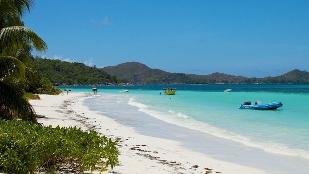 A beach with clear turquoise water, white sand, and boats. - L'Hirondelle (Praslin Island)