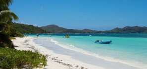 Una playa con agua turquesa cristalina, arena blanca y barcos.