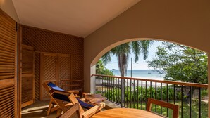 A wooden deck with a table and chairs, overlooking a beach with palm trees and a fence. - L'Hirondelle (Praslin Island)