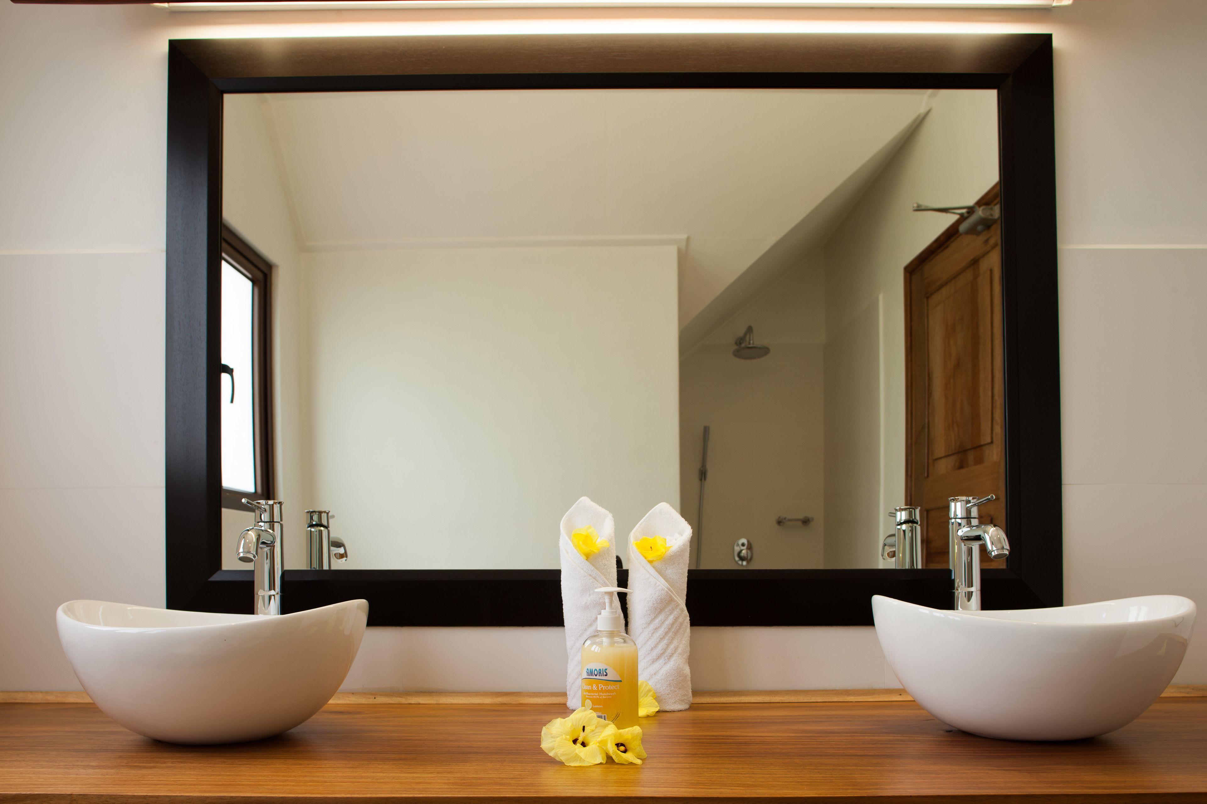 A bathroom with two white vessel sinks, a large mirror, and a bottle of shampoo.