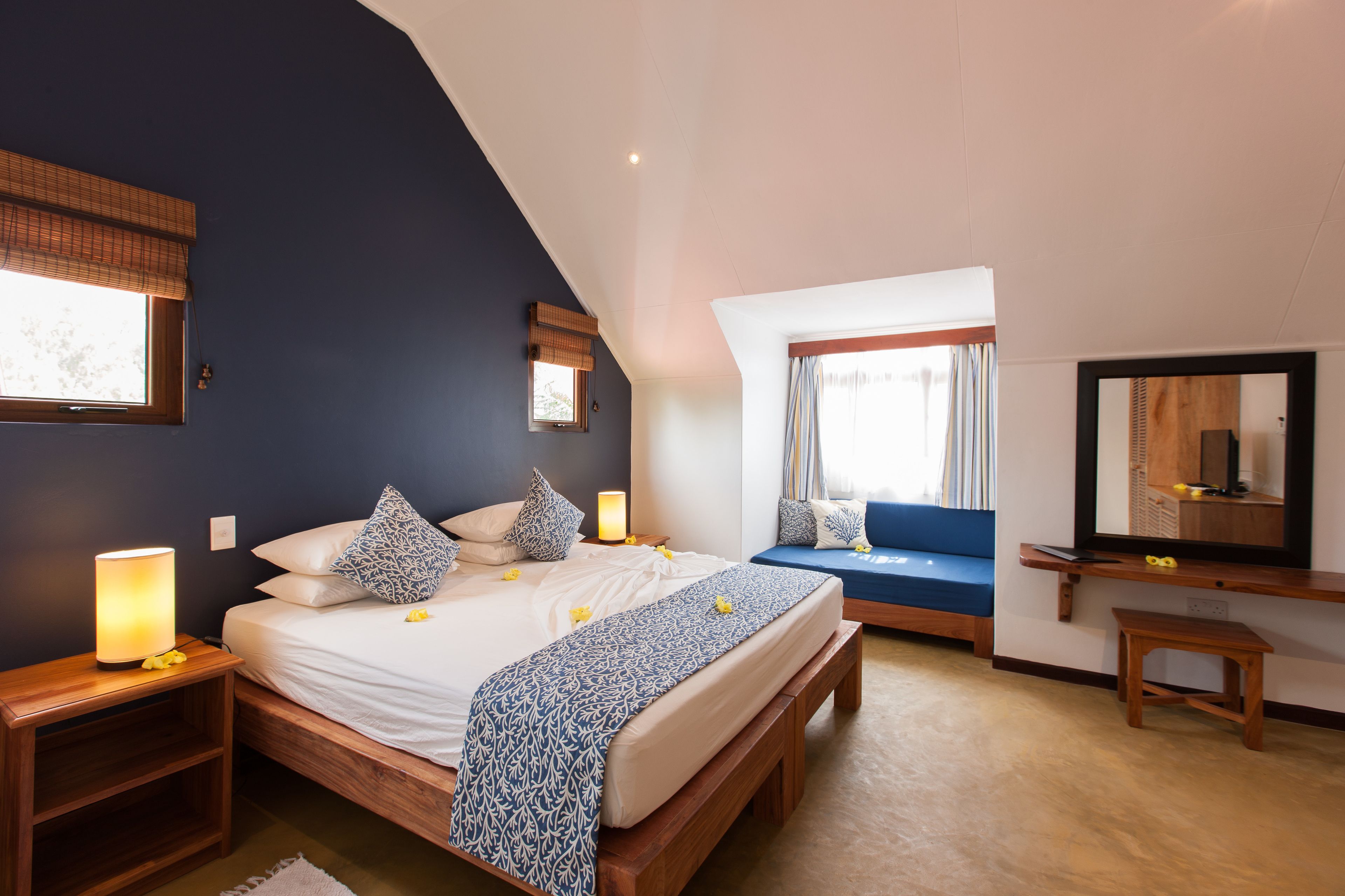 A bedroom with a large bed, bedside tables, a bench, a window with curtains, and a mirror.