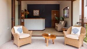 A room with two wicker chairs, a wooden coffee table, and a reception desk. - L'Hirondelle (Praslin Island)