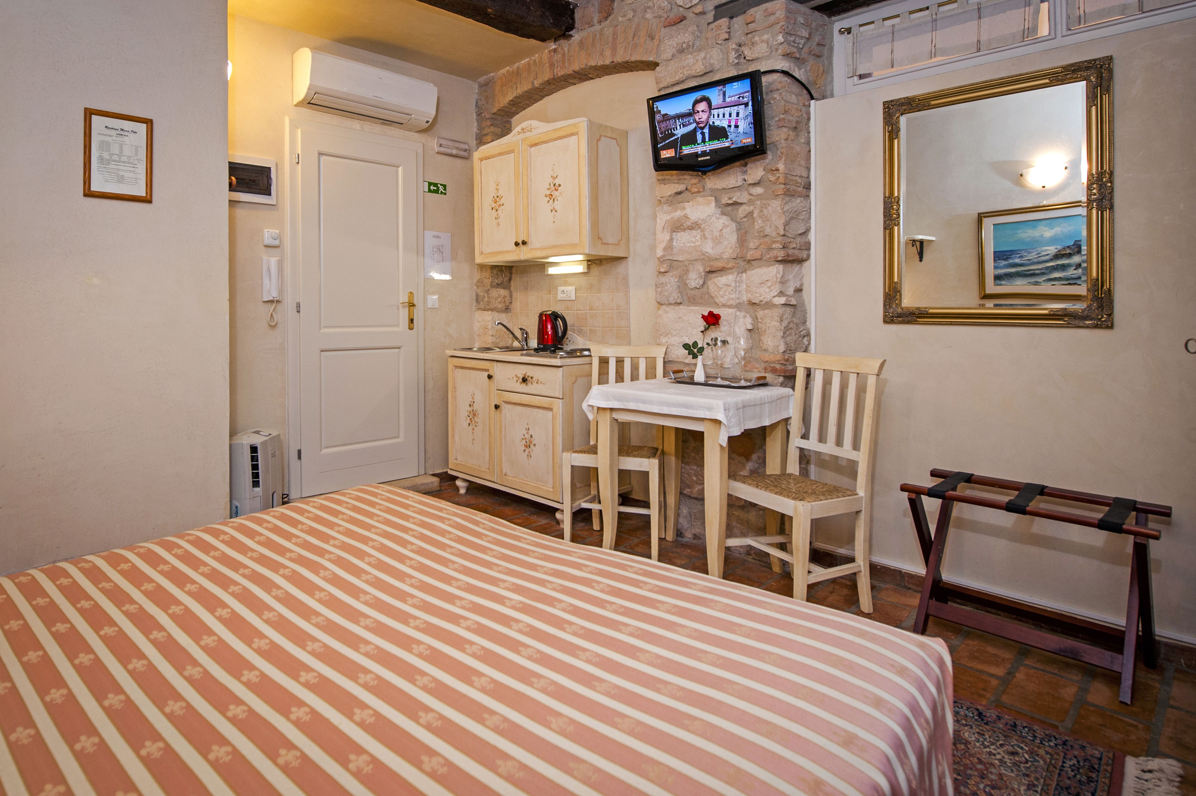 A hotel room with a bed, a small table with chairs, a television mounted on the wall, and a wooden bench.