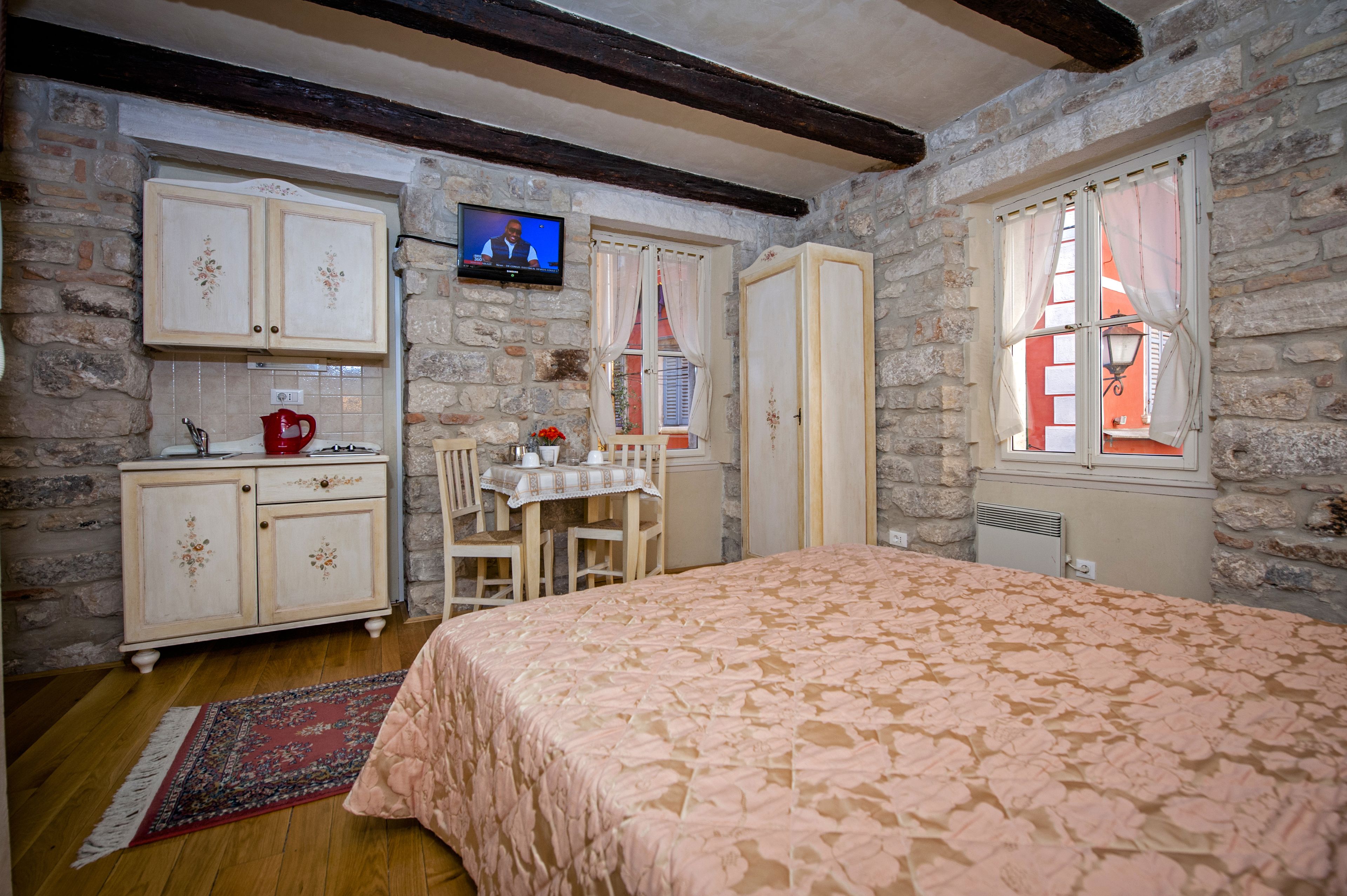 Une pièce chaleureuse avec un lit, une petite table entourée de chaises, un téléviseur et des murs en pierre.