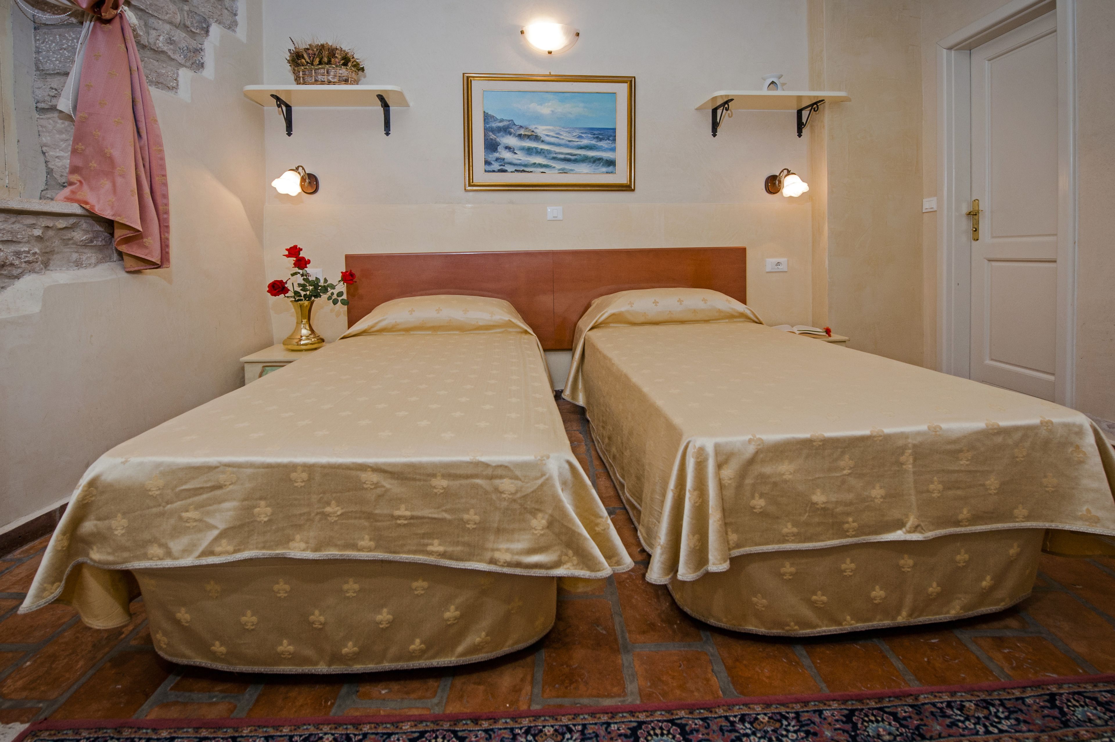 A room with two beds, a wooden headboard, a painting above the beds, and a door to the right.