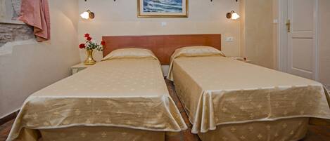 A room with two beds, a wooden headboard, a painting above the beds, and a door to the right.