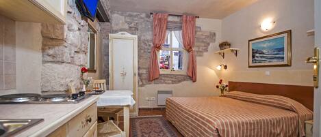 A bedroom with a bed, a desk, a chair, a TV, and a window with curtains.