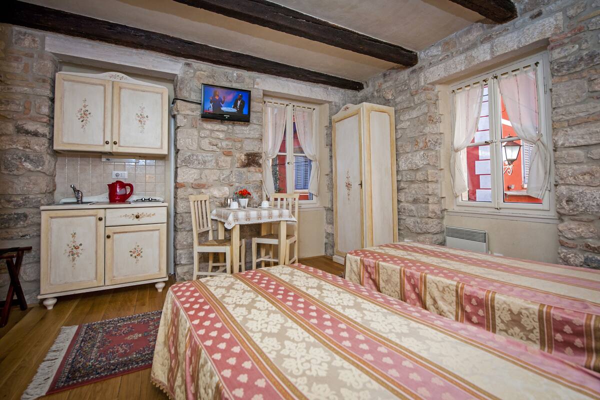 A traditional room with stone walls, wooden beams, a dining area with a table and chairs, and two beds with patterned bedding.