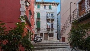 Une rue étroite avec un scooter garé sur le trottoir, des immeubles dotés de balcons et un ciel dégagé.