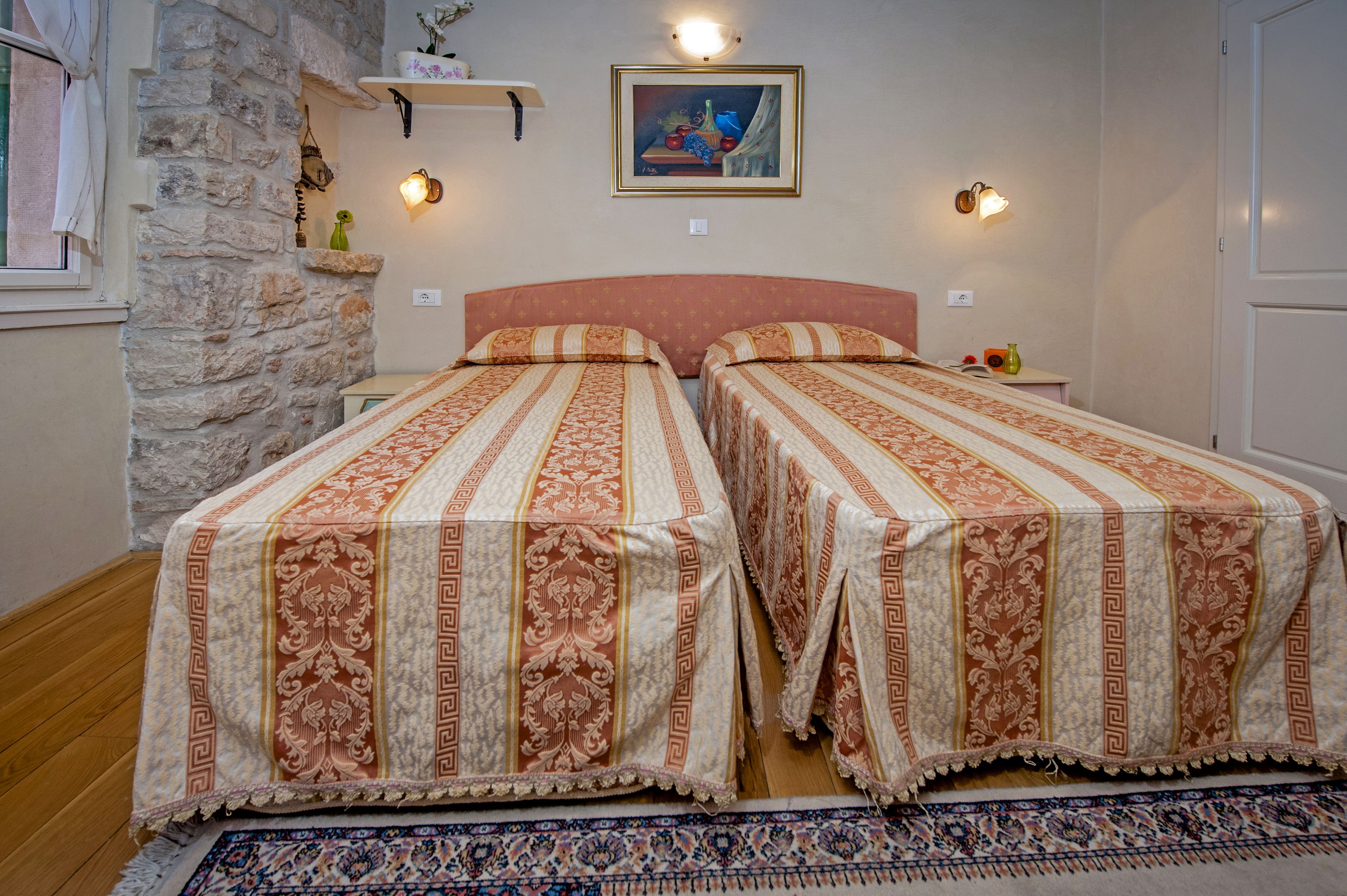 A room with two beds, a stone wall, a painting, and a rug.