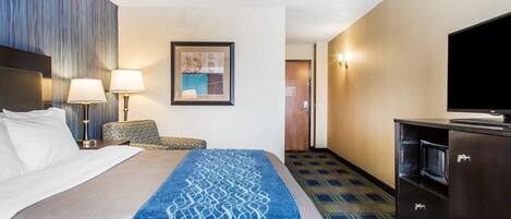 A hotel room with a bed, two bedside lamps, a chair, a television, and a minibar.