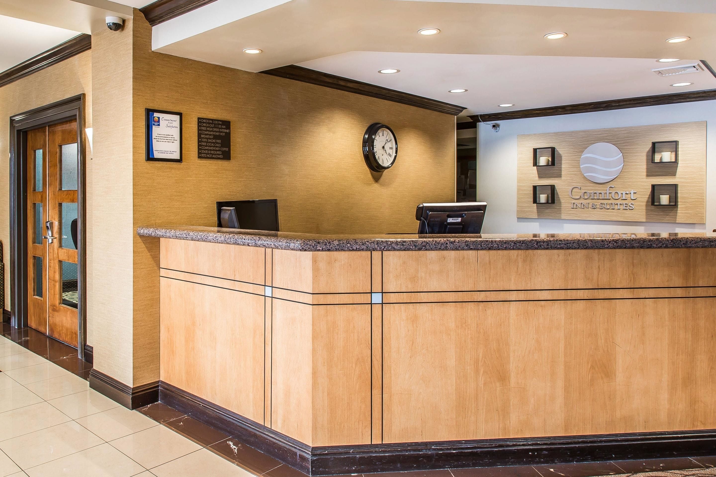 A hotel reception area with a wooden reception desk, a clock, and a sign for Comfort Inn & Suites.