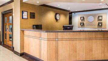 A hotel reception area with a wooden reception desk, a clock, and a sign for Comfort Inn & Suites.