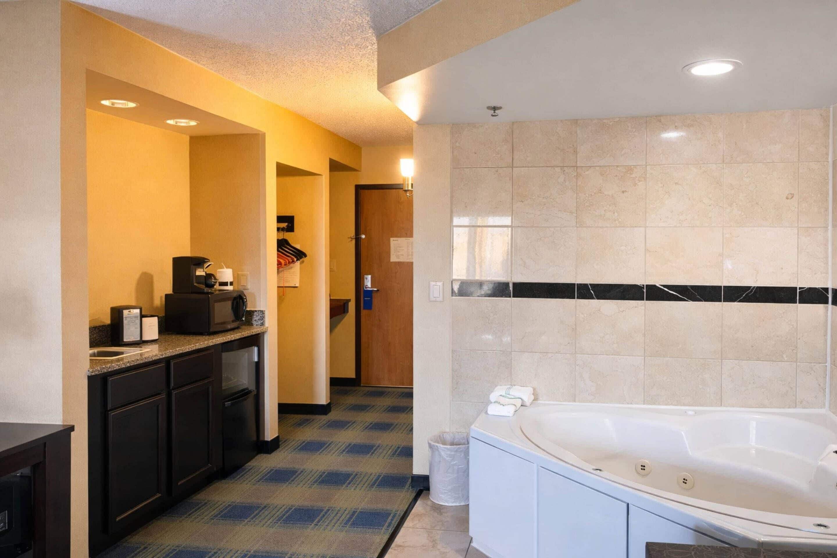 A hotel bathroom with a bathtub, a coffee machine, and a trash can.