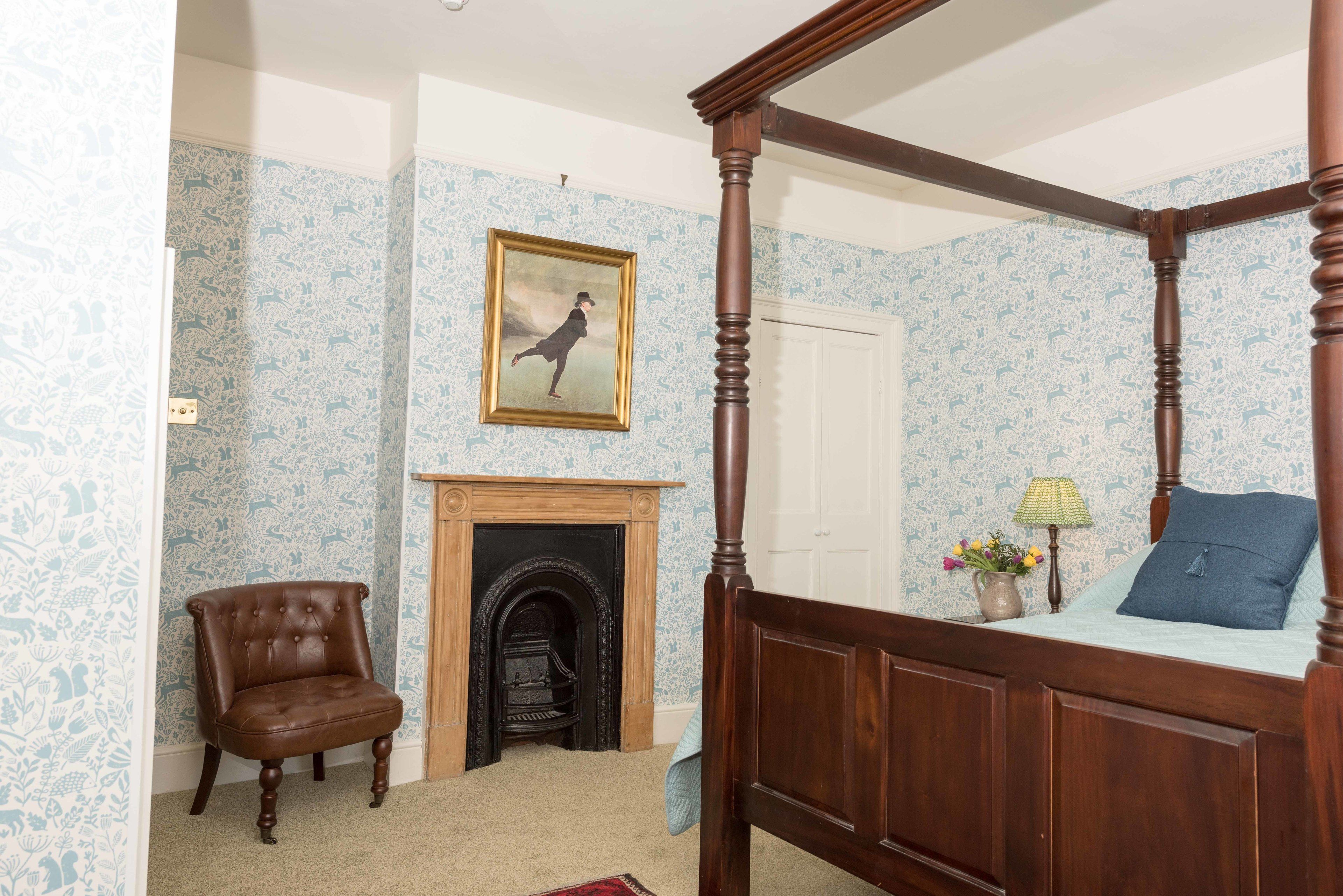 A four-poster bed, a leather armchair, a fireplace, and a framed picture on the wall.