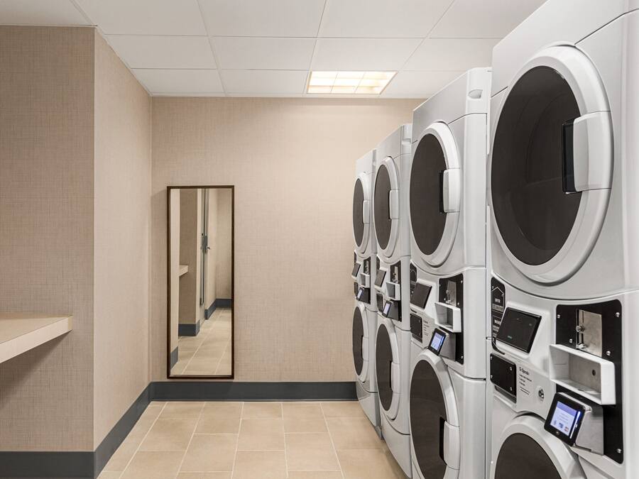 Un cuarto de lavandería con varias lavadoras, un espejo y piso de baldosas.