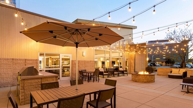 Un patio al aire libre con mesas, sillas, una parrilla y luces colgantes.