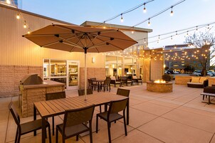 Un patio al aire libre con mesas, sillas, una parrilla y luces colgantes.