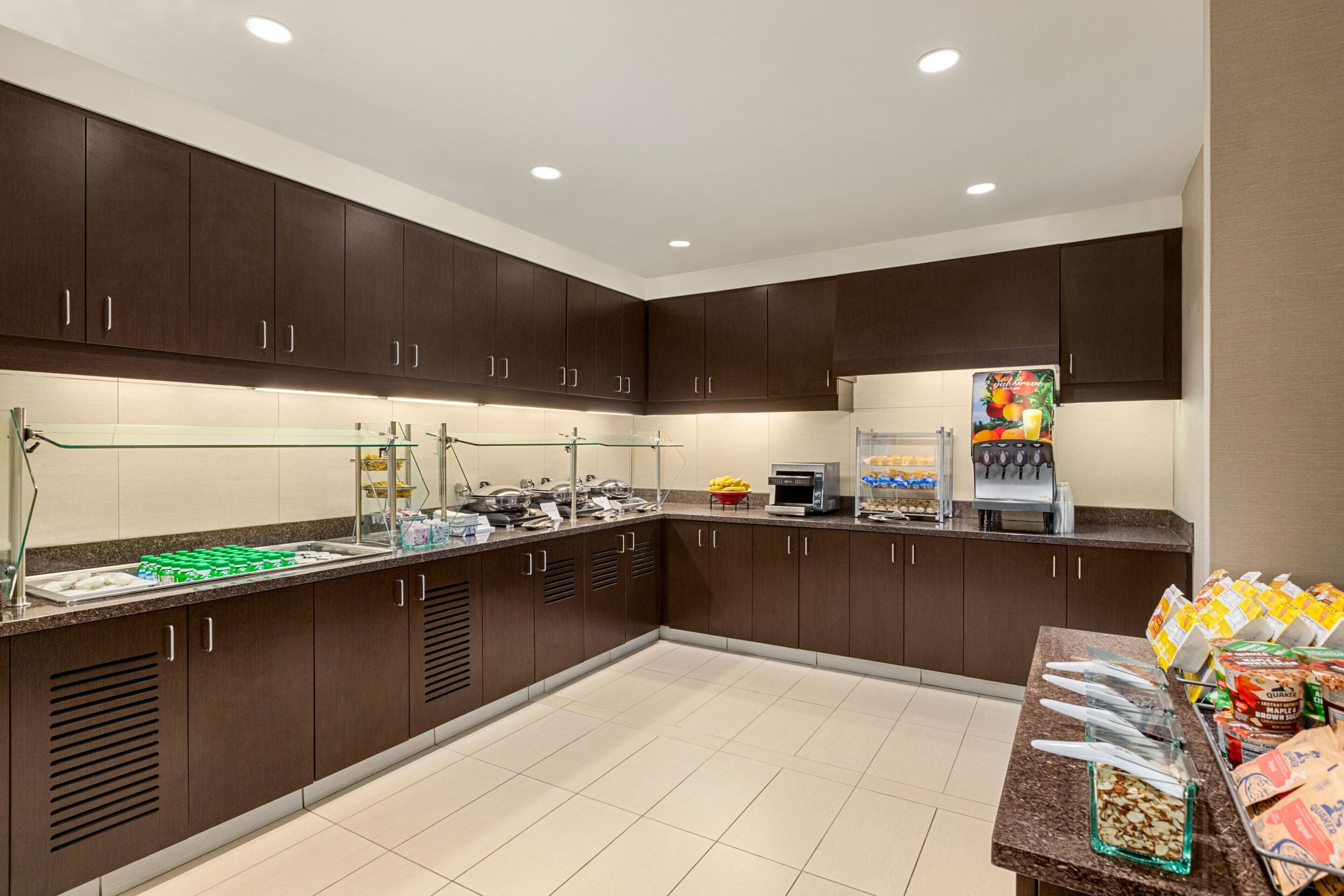A modern kitchen with dark wooden cabinets, a glass counter, and various food items.
