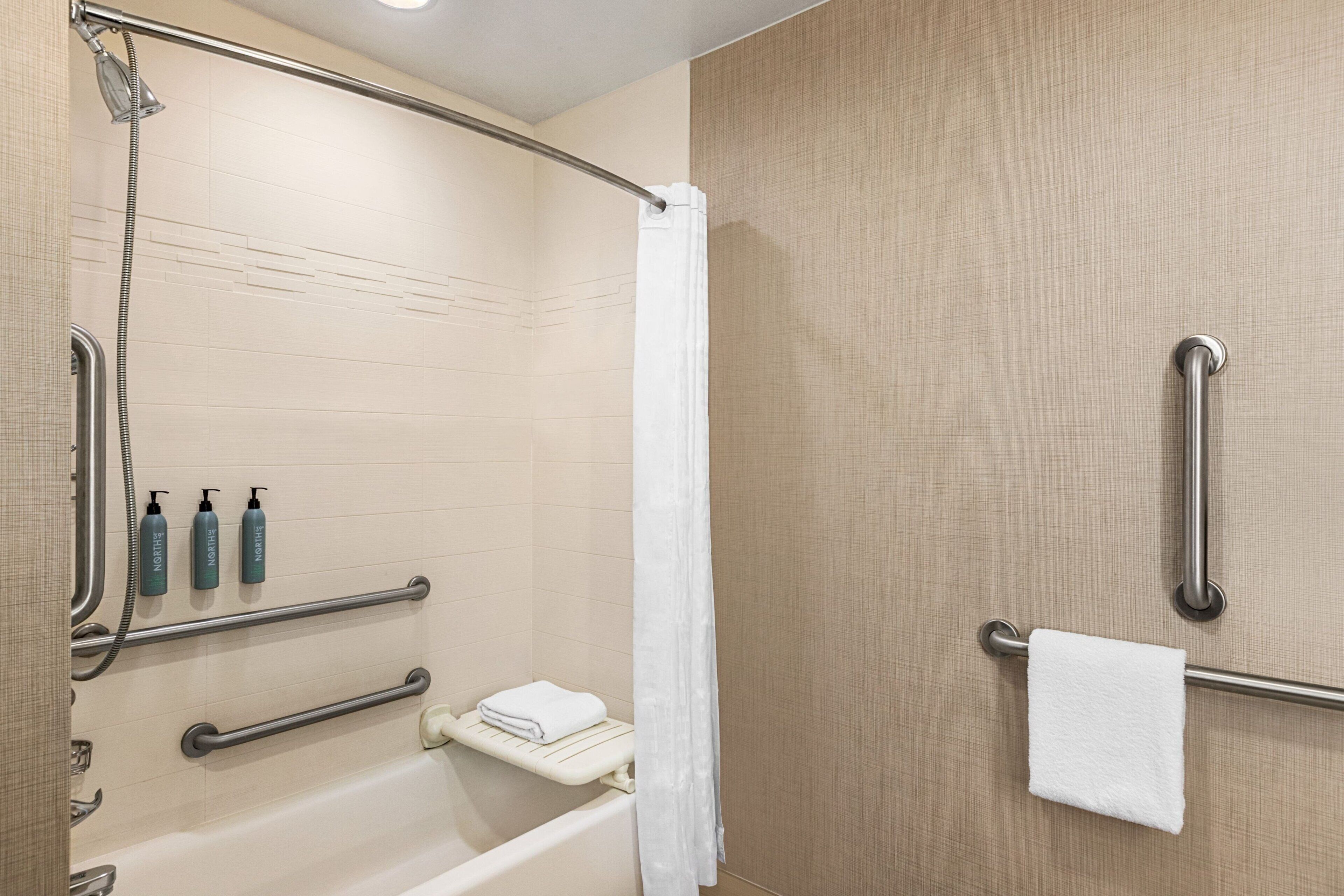 A bathroom with a shower, grab bars, a towel rack, and a hand dryer.