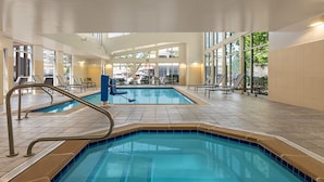 Una piscina interior con paredes de vidrio transparente, borde de azulejos azules y ambiente luminoso.