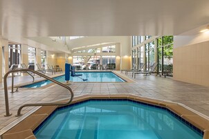 Una piscina interior con paredes de vidrio transparente, borde de azulejos azules y ambiente luminoso.