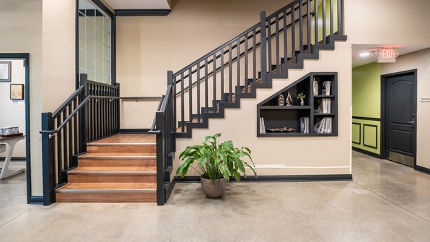 A staircase with black railings and wooden steps, a potted plant, and a bookshelf with books and decorative items. - The Hotel Sync (Bowling Green)