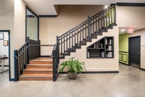 A staircase with black railings and wooden steps, a potted plant, and a bookshelf with books and decorative items. - The Hotel Sync (Bowling Green)