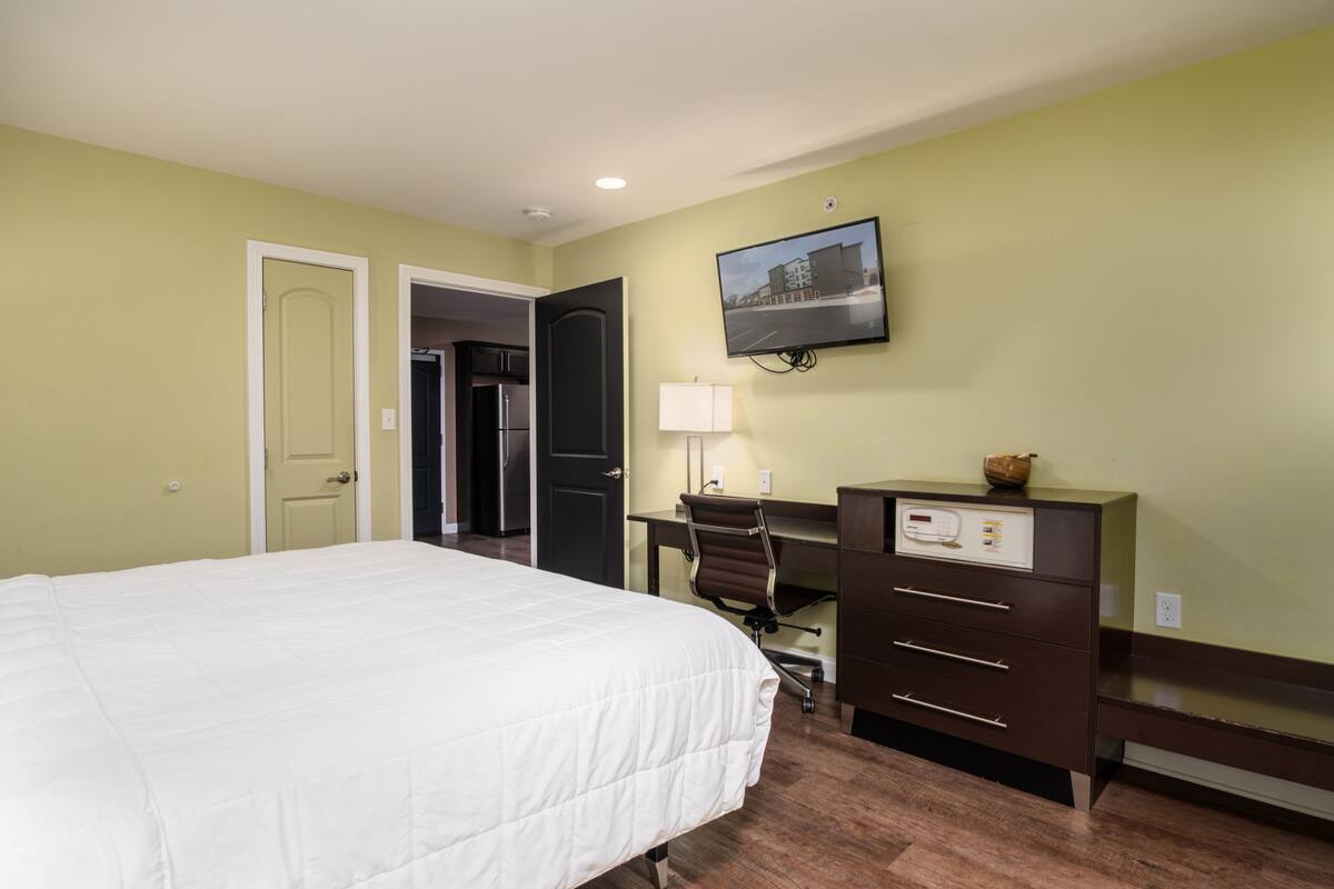 A hotel room with a bed, a desk, a chair, a dresser, and a television on the wall.