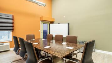 A conference room with a long table, six chairs, a whiteboard, and a window with blinds.