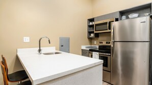 A compact kitchen with a white countertop, stainless steel appliances, and a wooden chair. - The Hotel Sync (Bowling Green)