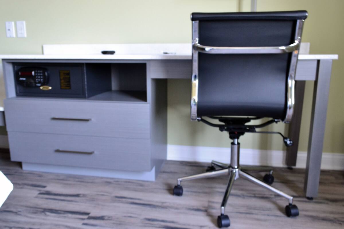 A modern office desk with a black office chair, a drawer unit, and a control panel.