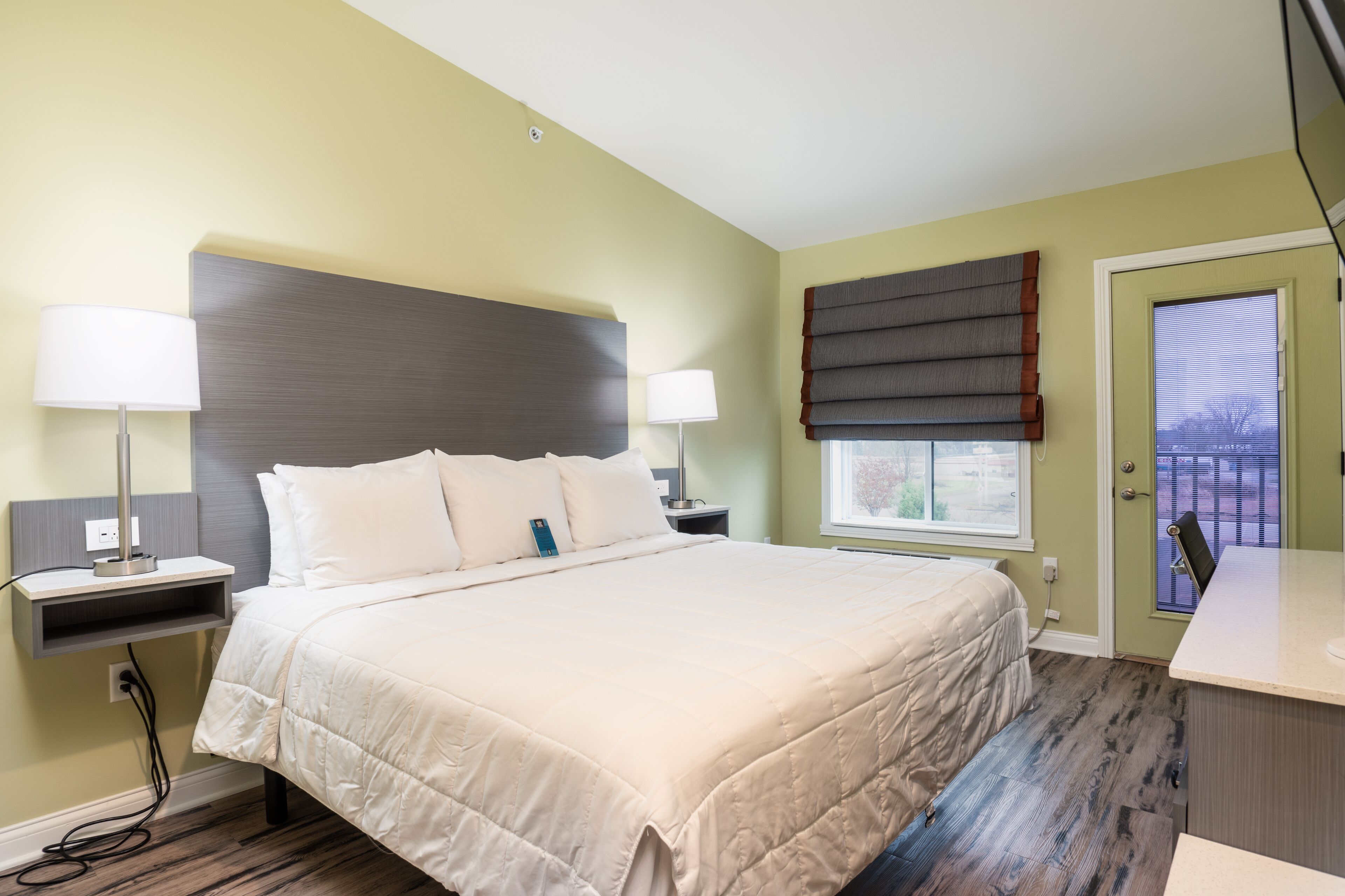 A neatly arranged bedroom with a large bed, bedside tables, a nightstand, and a window with blinds.