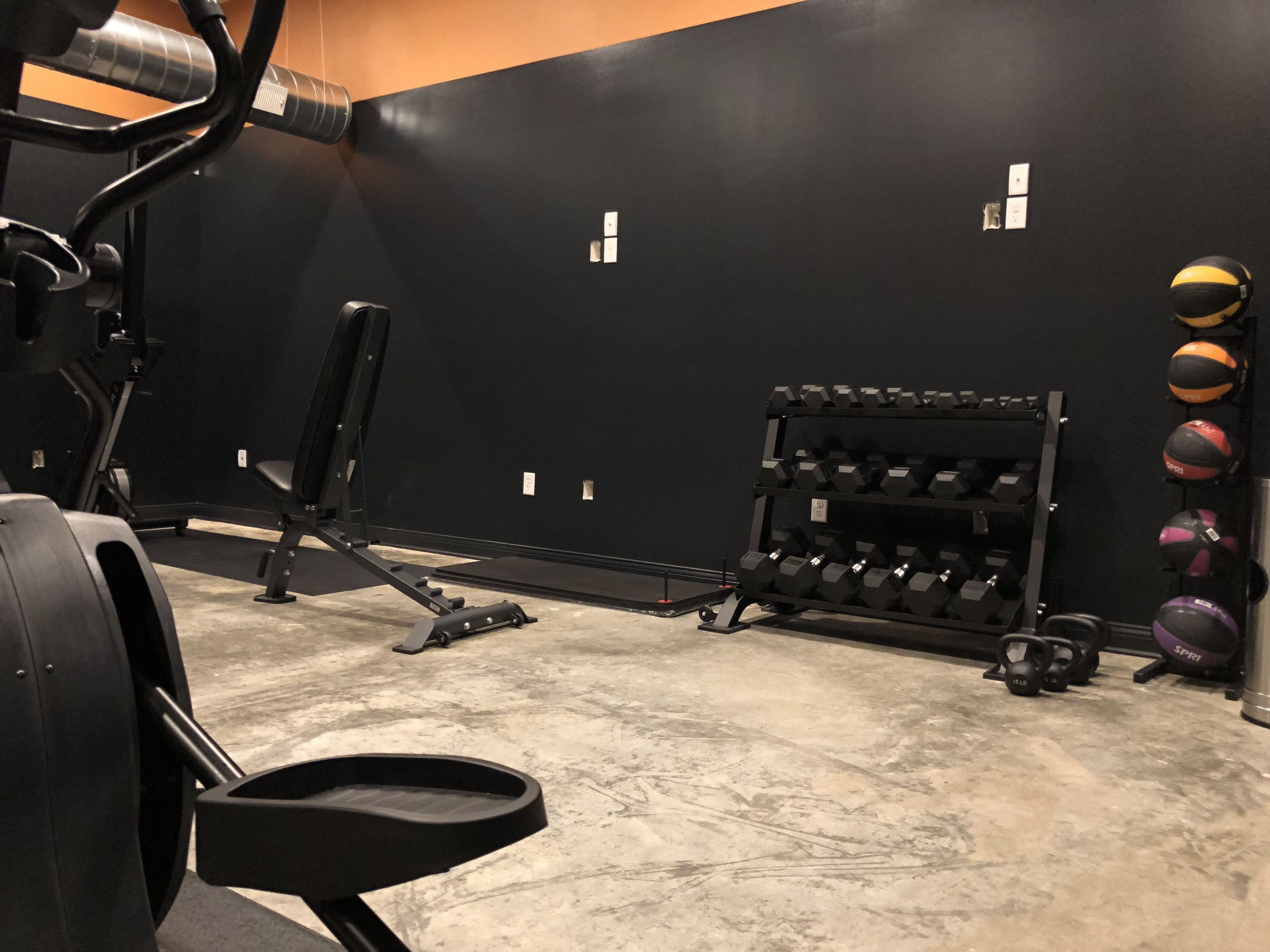 A gym with weightlifting equipment, a bench, and a rack of dumbbells.